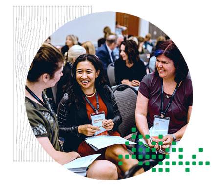 A group of three women smiling and having a conversation in a conference setting.